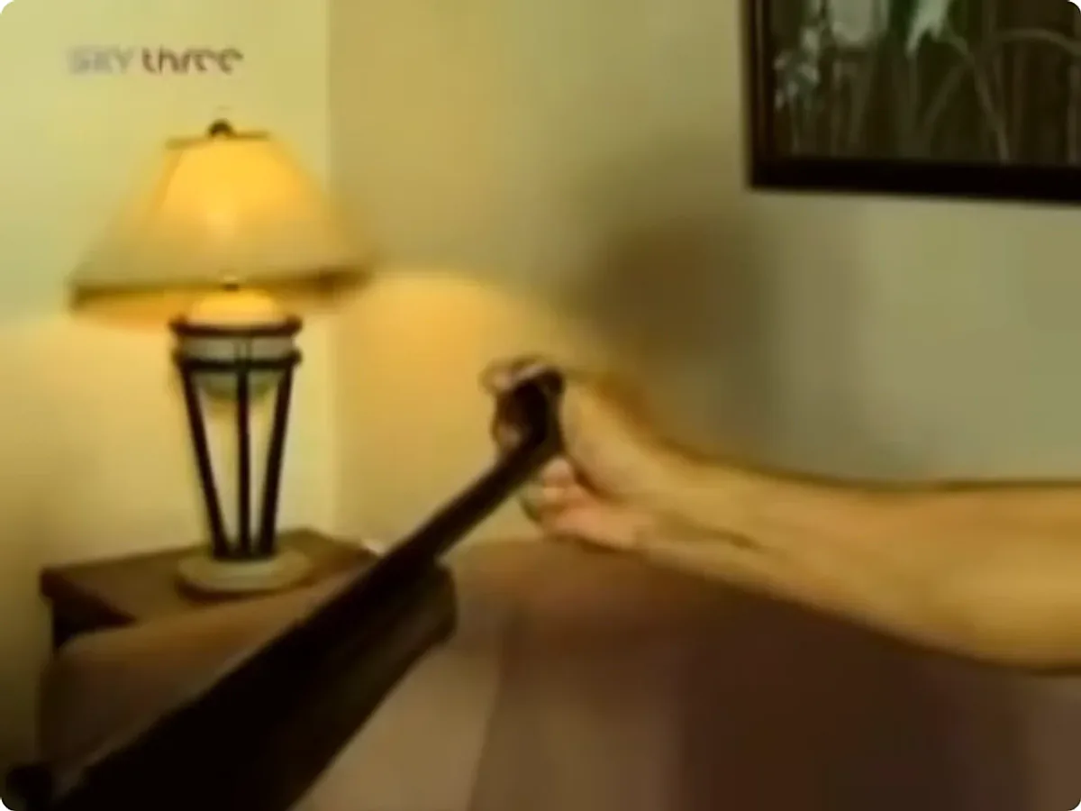 A broadcast still: an air rifle barrel aimed at close range at an outstretched open hand.