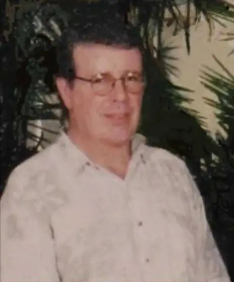 Jim McMillan, an older man in glasses and a pale patterned shirt, photographed in front of foliage.