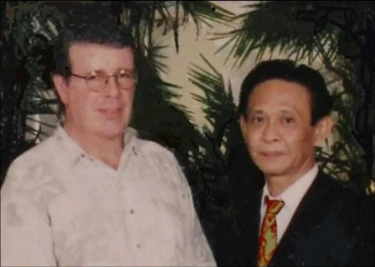Jim McMillan standing beside John Chang, both facing the camera, in front of a painted screen of foliage.