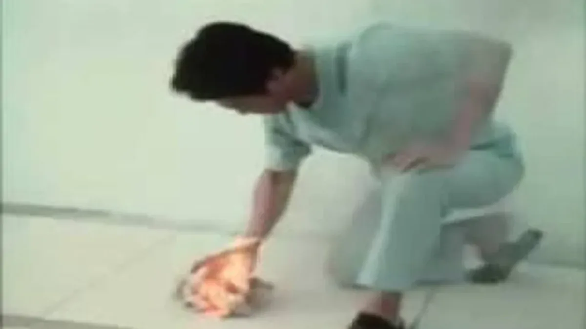 A still from the 1988 Ring of Fire footage: John Chang crouching over a tiled floor with paper alight beneath his hand.