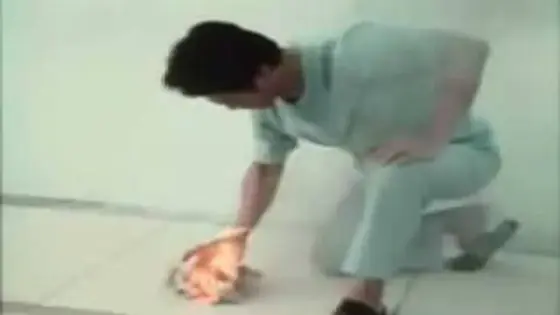 A still from the 1988 Ring of Fire footage: John Chang crouching over a tiled floor with paper alight beneath his hand.